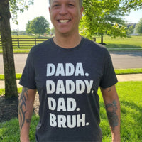 Load image into Gallery viewer, Dada. Daddy. Dad. Bruh. Everyday Tee in dark grey heather, worn by a real dad outdoors